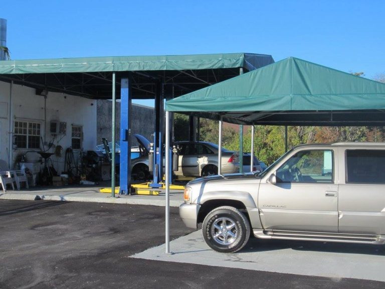 An outdoor auto service area shows a canopy-covered bay with a vehicle on a lift and a parked SUV.
