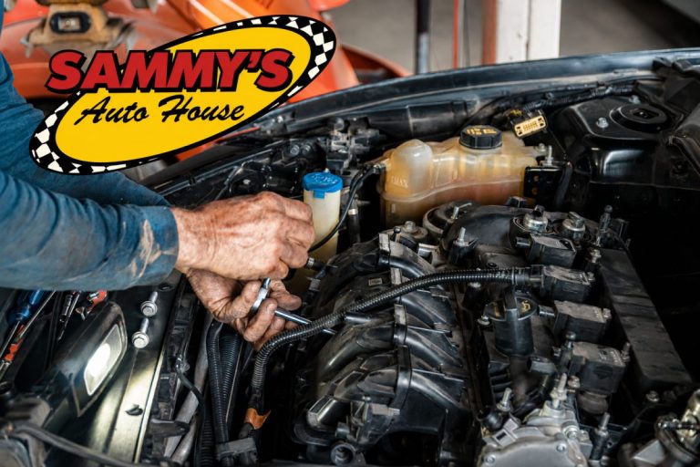 A person's hands using a wrench to work on a car engine under an open hood with the Sammy's Auto House logo visible.