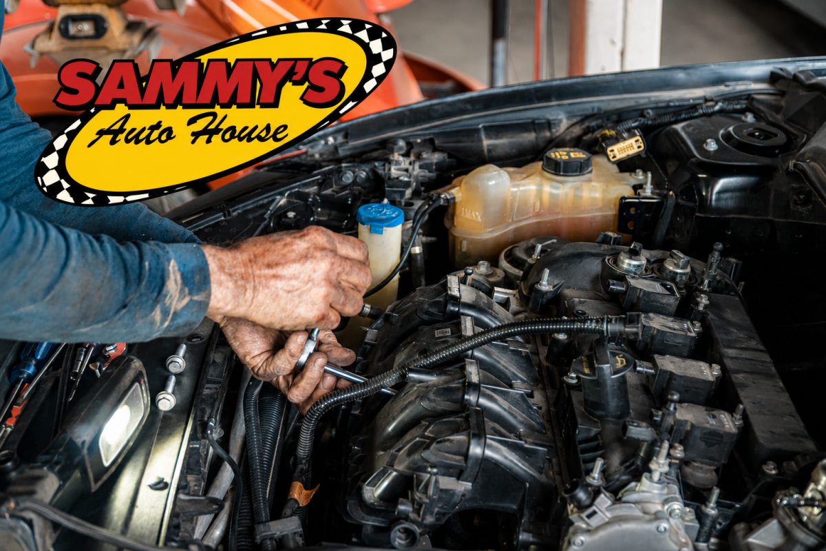 A person's hands using a wrench to work on a car engine under an open hood with the Sammy's Auto House logo visible.